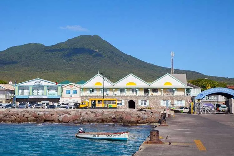 The Charlestown waterfront on Nevis, with harbour buildings below Nevis Peak and a small open boat moored at the pier.
