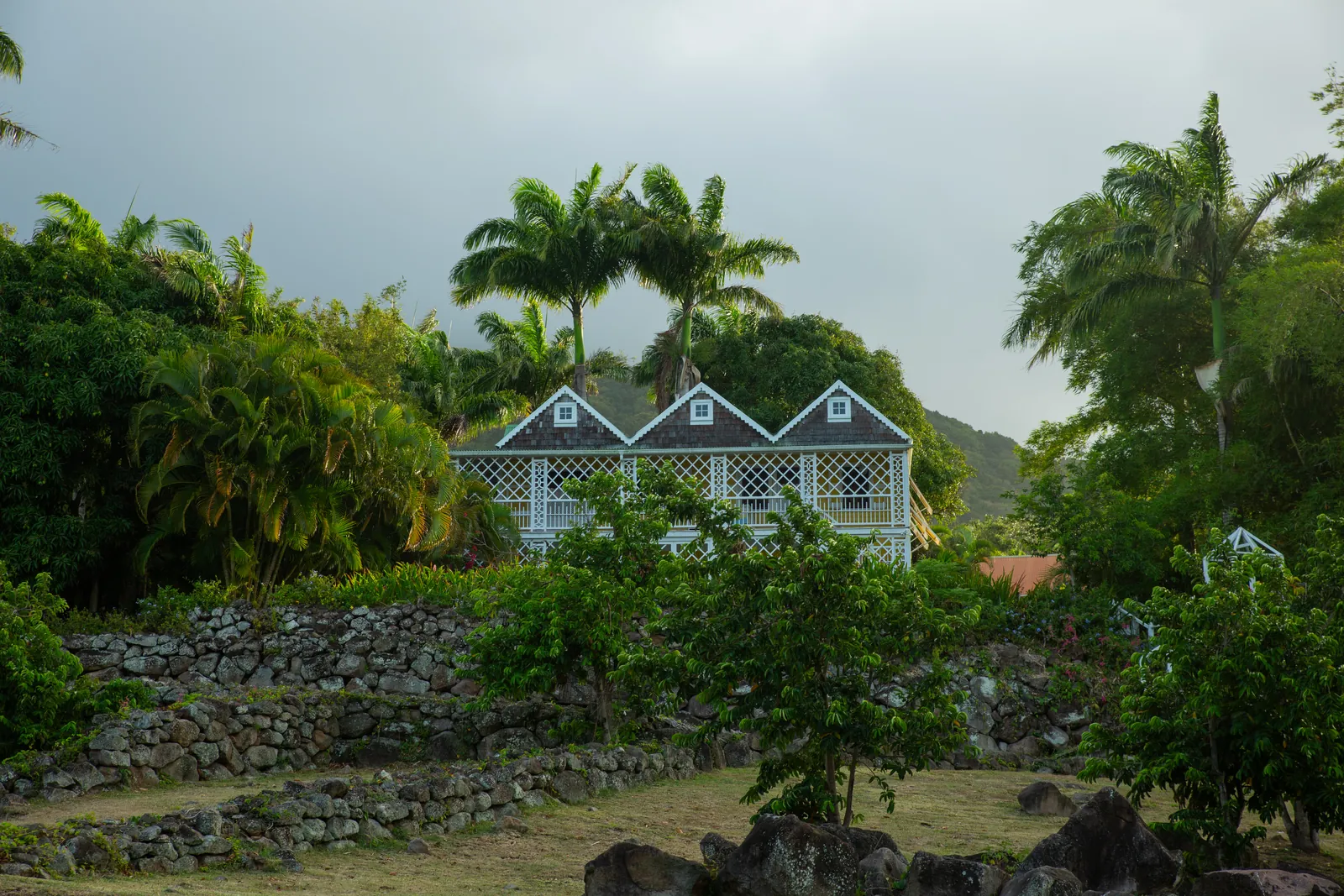 A white triple-gabled timber cottage with lattice veranda standing above dry-stone retaining walls on the Hermitage estate