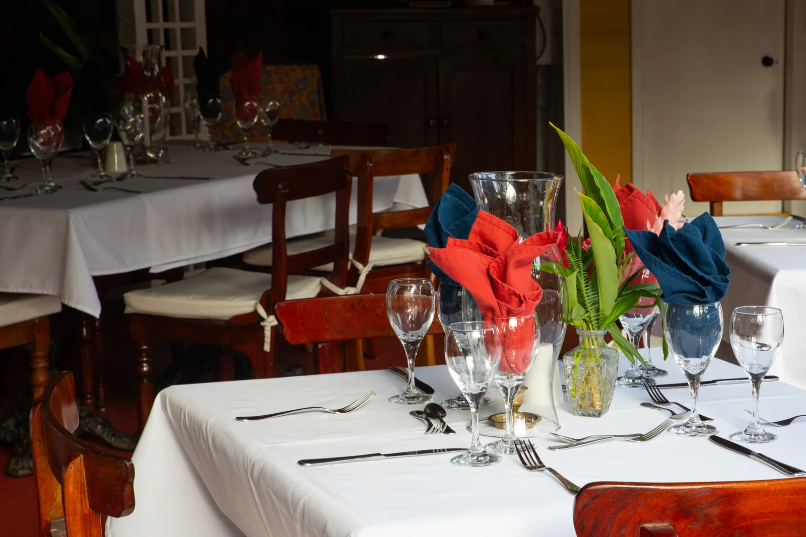 Tables laid with white linen and mahogany chairs in the Great House dining rooms at Hermitage Nevis