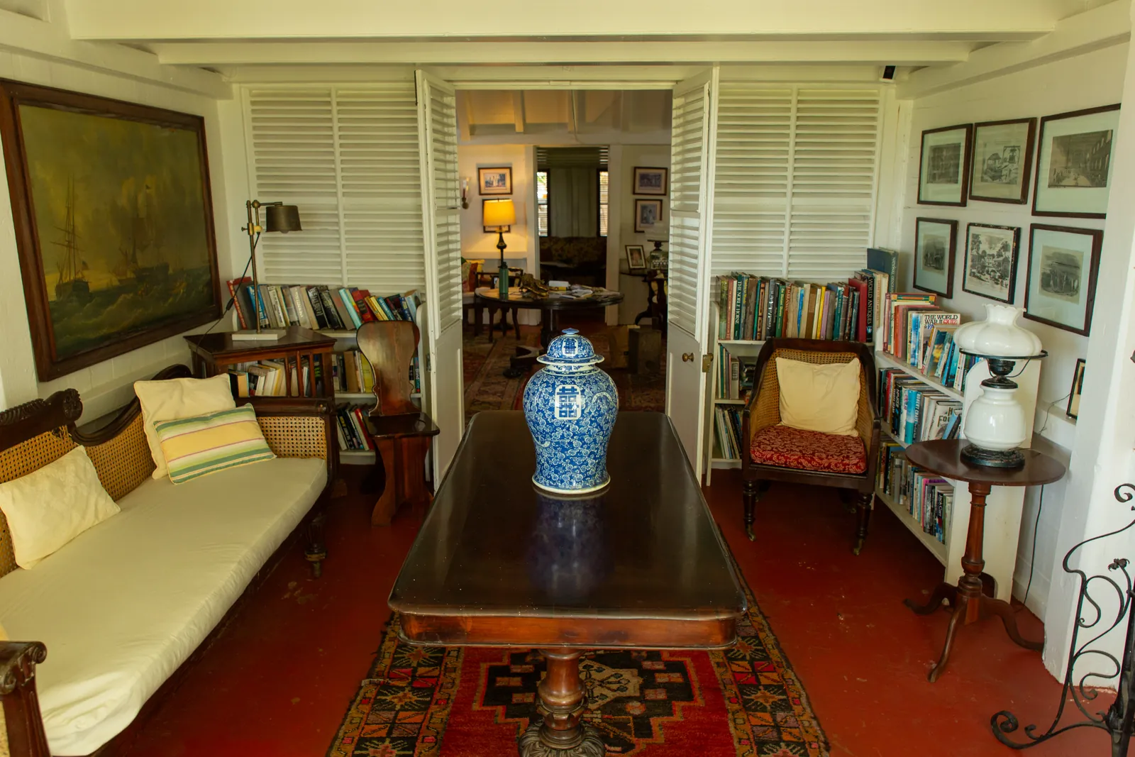 The historic sitting room and library inside the Great House at Hermitage Nevis, with a white daybed, ginger jar and a ship painting