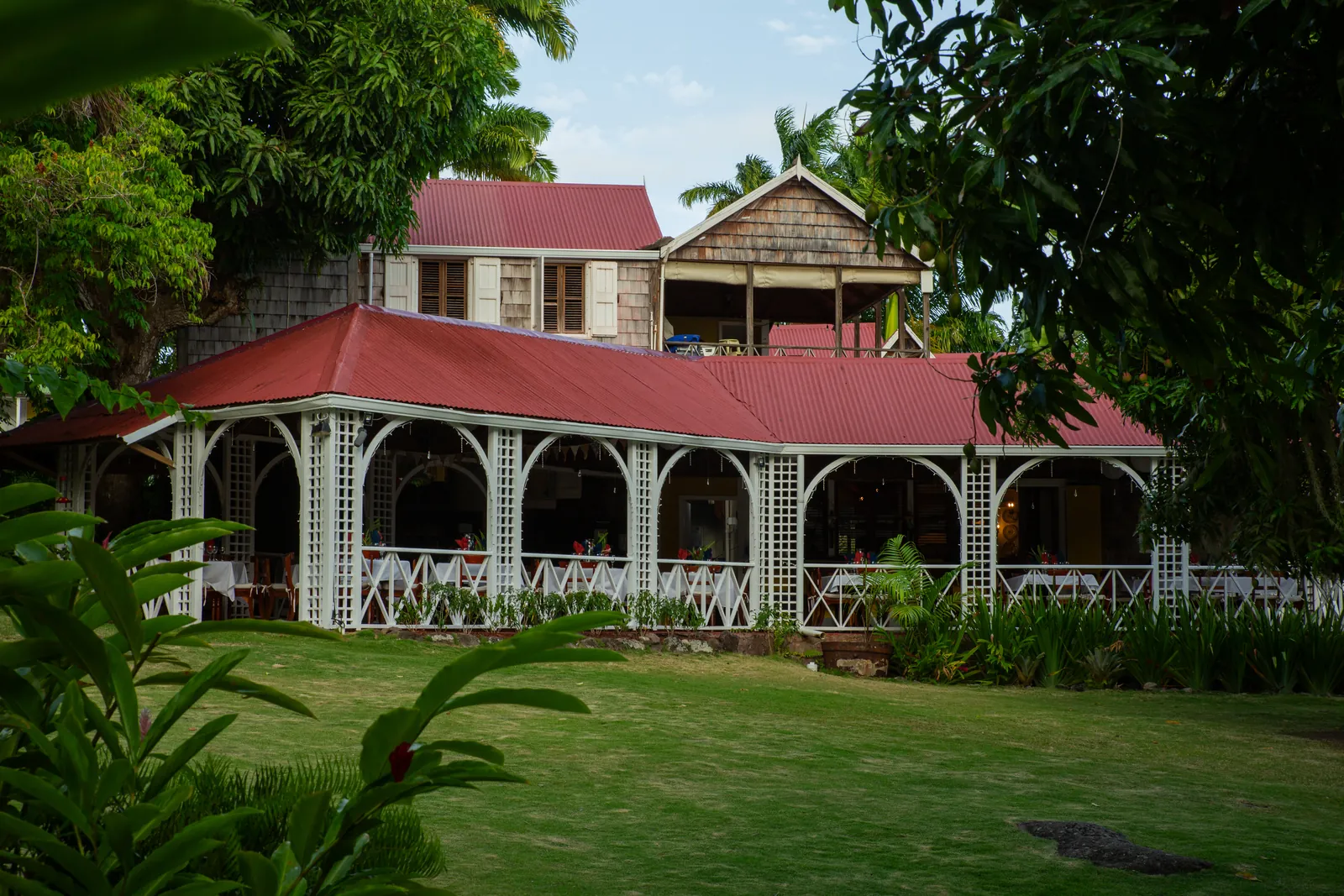The Great House at Hermitage Nevis across its lawn, its long white gingerbread veranda under a red roof and shingled upper storey.