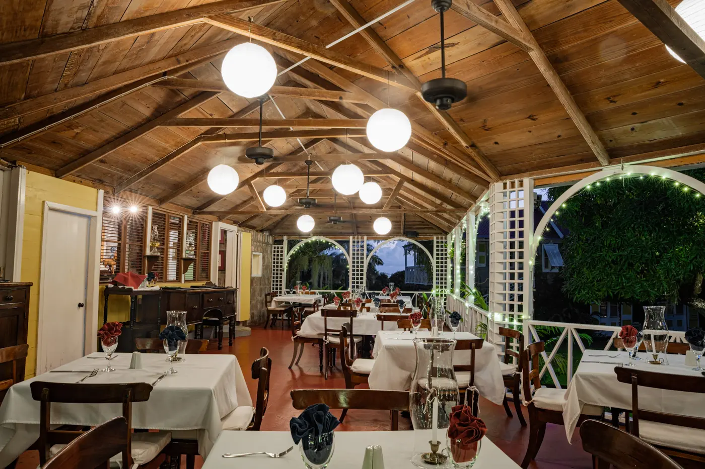 The restaurant dining room at Hermitage Nevis, beneath its timber ceiling, set with white-linen tables