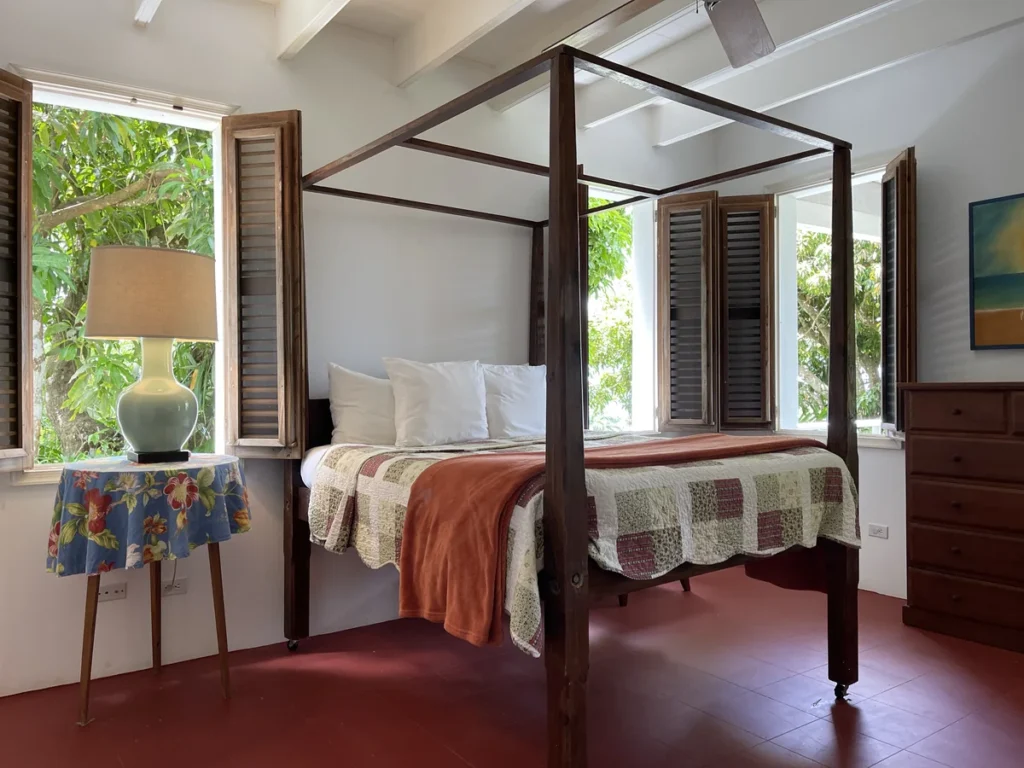 Bedroom at Rose Villa with a four-poster bed, ceiling fan and shuttered windows onto the garden.
