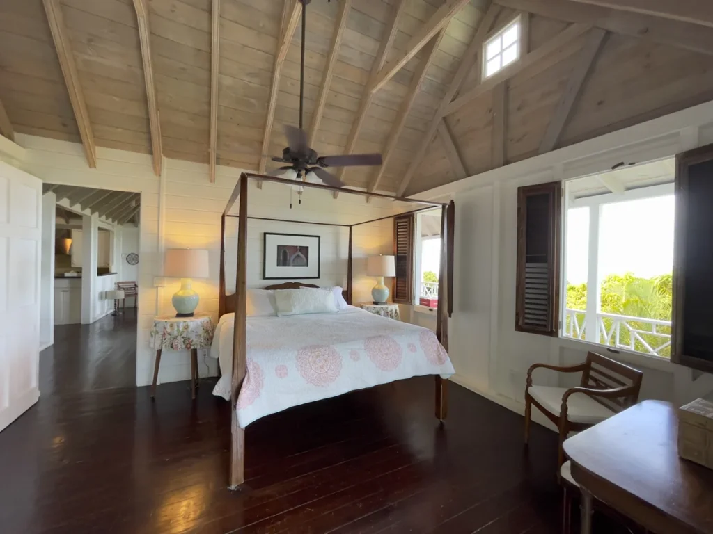 Bedroom at Rose Villa with a four-poster bed beneath an open timber ceiling and a polished wood floor.