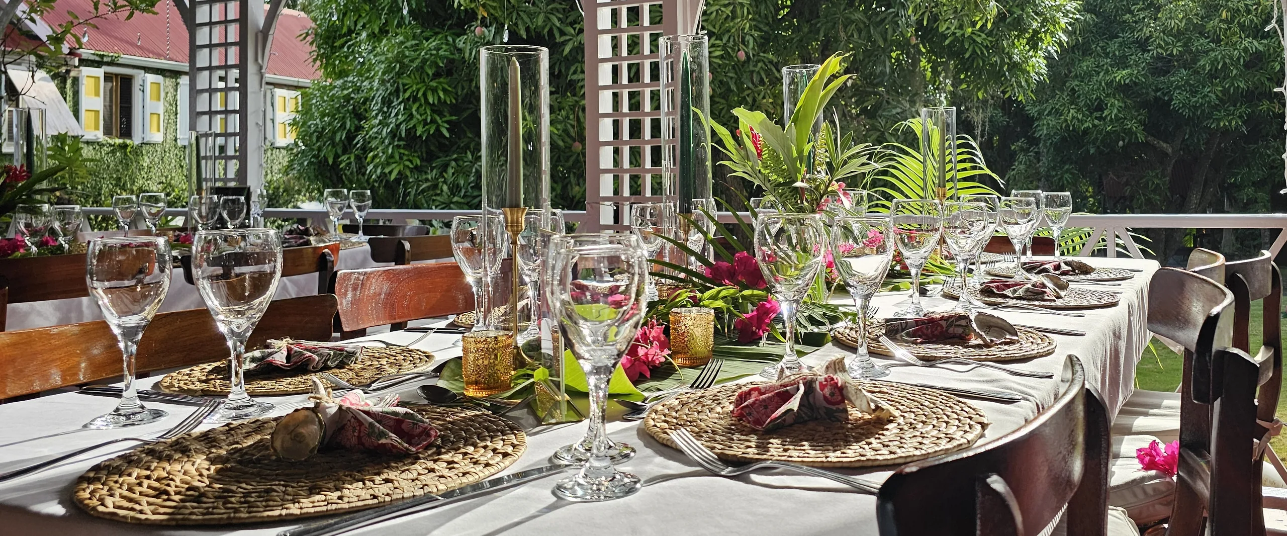 A long table laid with glasses, candles and flowers at Hermitage Nevis, with a red-roofed house beyond