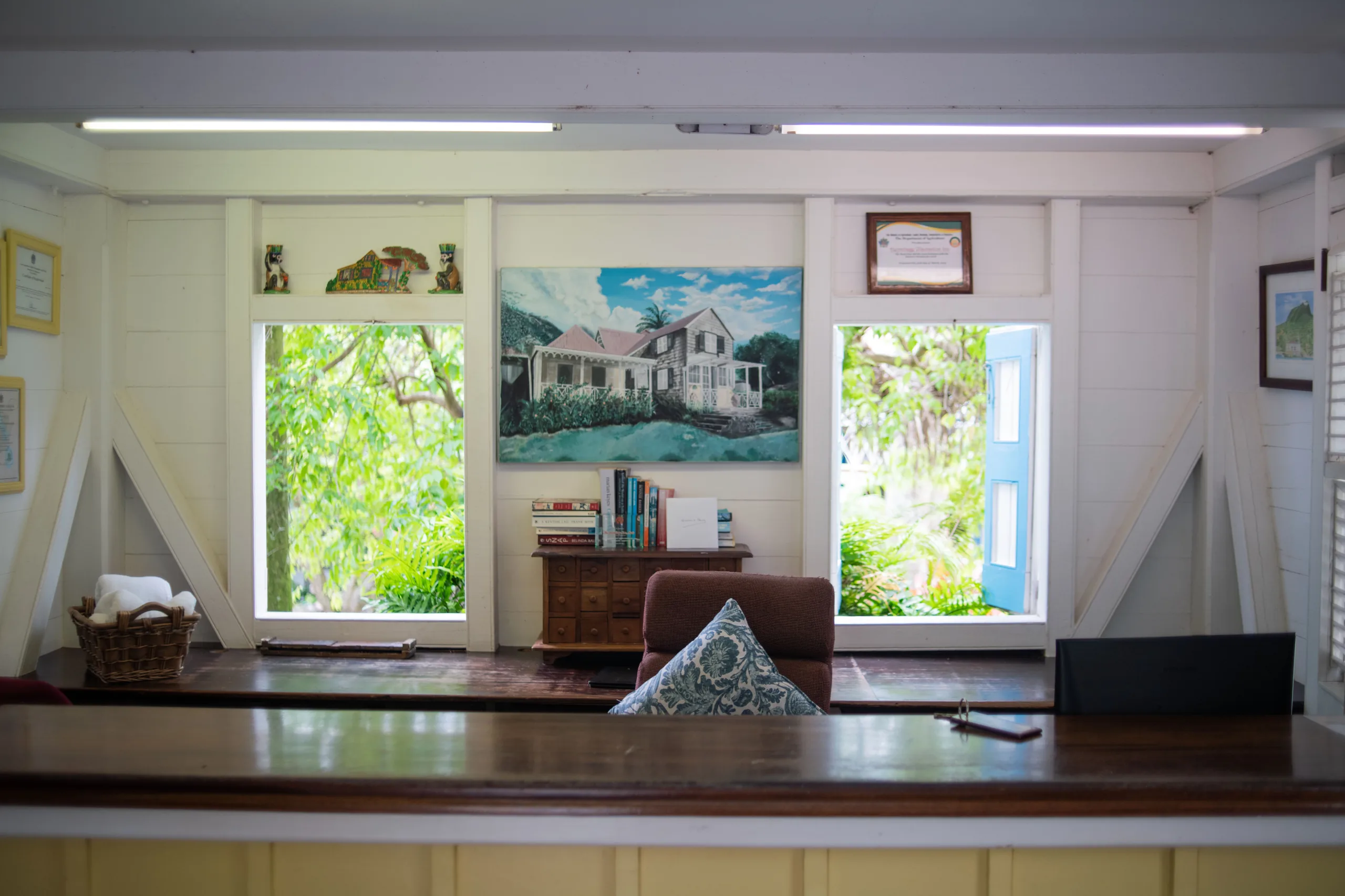 Office desk at Hermitage Nevis with a painting of a shingled house on the wall and open windows onto the garden